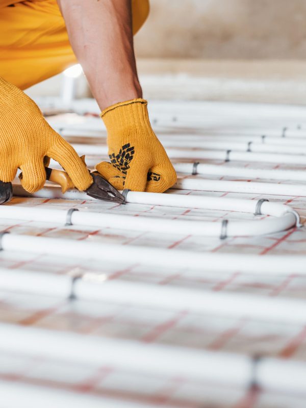 Close up view. Worker in yellow colored uniform installing underfloor heating system.